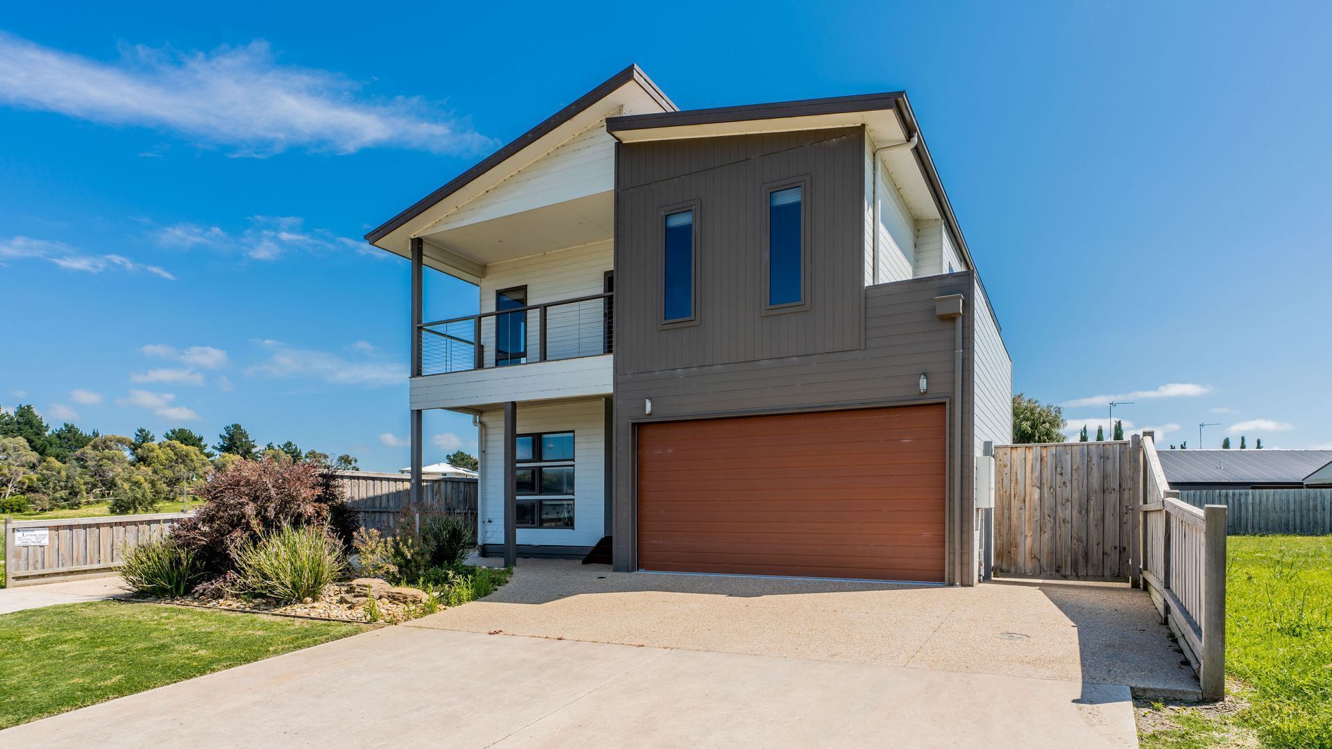 A modern two-story house with a garage, a balcony on the upper floor, and a well-maintained lawn.