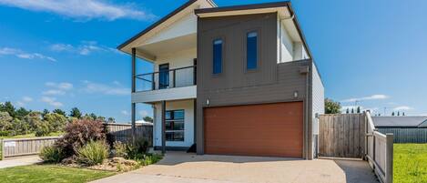 A modern two-story house with a garage, a balcony on the upper floor, and a well-maintained lawn.