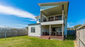 Une maison à deux étages avec un balcon à l’étage supérieur, une véranda couverte au rez-de-chaussée et une cour arrière clôturée.