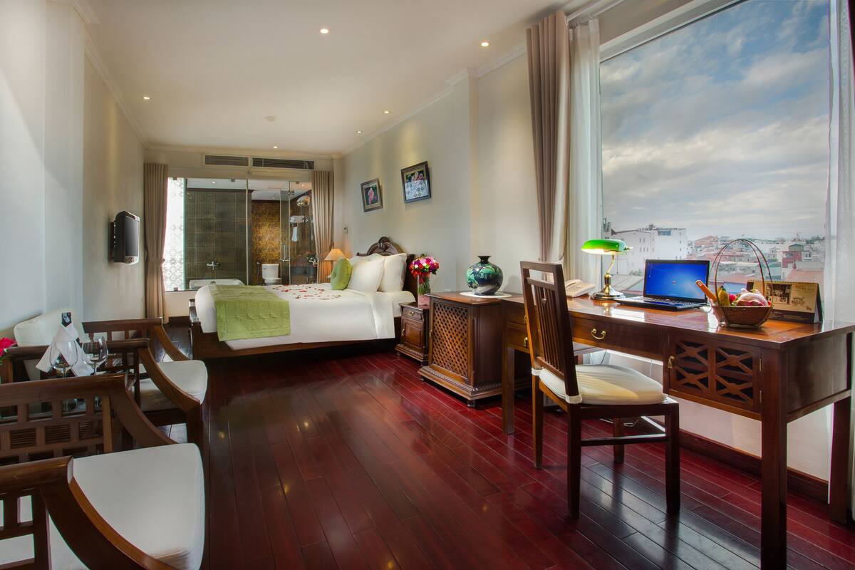 A hotel room with a bed, desk, chair, and a view of the city through the window.