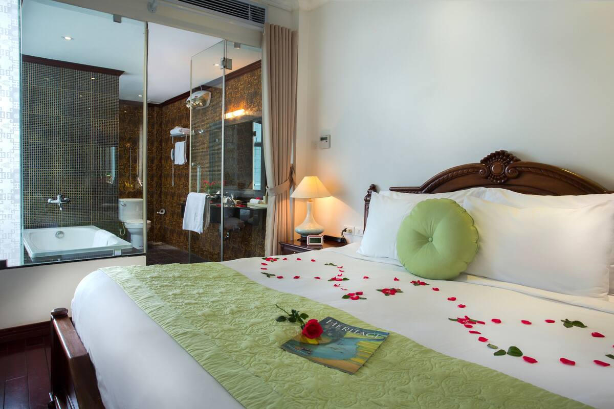 A hotel room with a large bed, a green pillow, and a book titled "Heritage" on the bed.