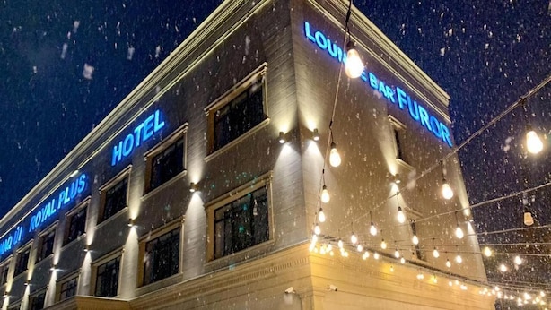 Un hotel con un cartel iluminado en azul que indica “HOTEL ROYAL PLUS” y “LOUIE BAR FUROR”.