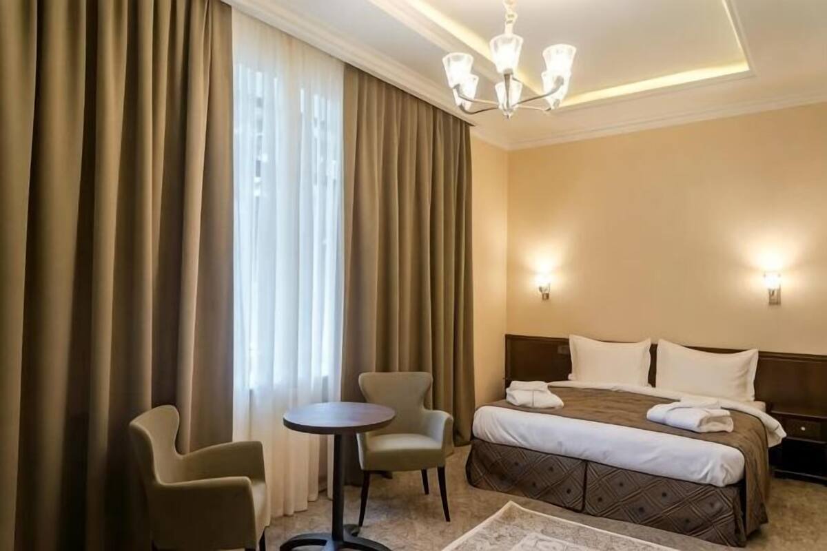 A hotel room with a bed, two chairs, a small table, and a chandelier.