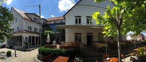 A courtyard with outdoor seating, a covered area, and a building with a white facade and red roof. - Hotel & Restaurant Grüner Baum (Krumbach)