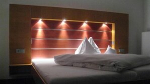 Una habitación de hotel con cama, cabecero de madera con luces y almohada blanca.