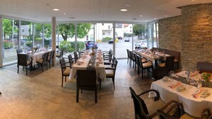 Un restaurante con varias mesas preparadas para comer, ventanas amplias que dan a la calle y una pared de piedra en un lateral.