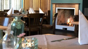Un restaurante con mesas dispuestas para comer, una chimenea al fondo y vistas al exterior a través de las ventanas.