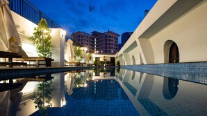 Una piscina con un riflesso limpido, circondata da un edificio bianco con finestre ad arco e un balcone.