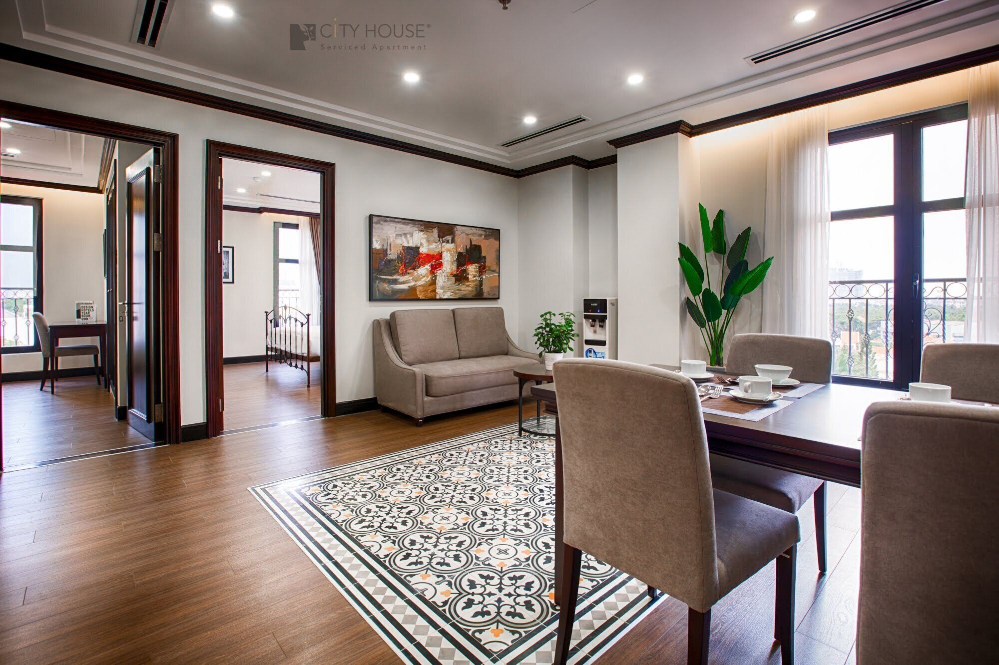 A modern serviced apartment with a dining area, a living room with a sofa, a large window with a view, and a decorative rug.