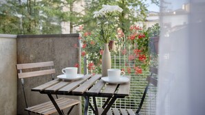 Ein Holztisch mit zwei weißen Tassen und Untertassen, einer Vase mit weißen Blumen und einer Bank.