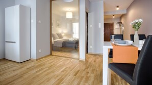 Ein modernes Hotelzimmer mit Holzboden, einem Bett mit grauem Kopfteil, einem weißen Kleiderschrank und einer Essecke mit Tisch und Stühlen.