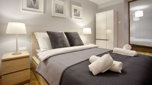 Ein modernes Hotelzimmer mit einem großen Bett, zwei Nachttischen mit Lampen, einem Kleiderschrank und gerahmten Bildern an der Wand.