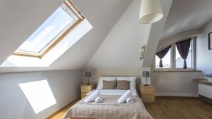 A bedroom with a skylight, a bed with towels, a nightstand, a lamp, and a window with curtains. - Apartament Amber Krakow (Kraków)
