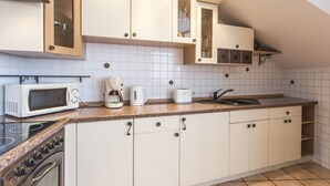 A modern kitchen with white cabinets, a granite countertop, a microwave, a coffee maker, and a stove. - Apartament Amber Krakow (Kraków)