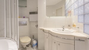 A modern bathroom with a glass shower enclosure, a toilet, a sink with a mirror, and a small shelf with toiletries. - Apartament Amber Krakow (Kraków)