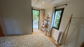 Une chambre avec une couvre-lit à motifs, une échelle en bois, une étagère avec des serviettes et une vue sur l’extérieur par une fenêtre.