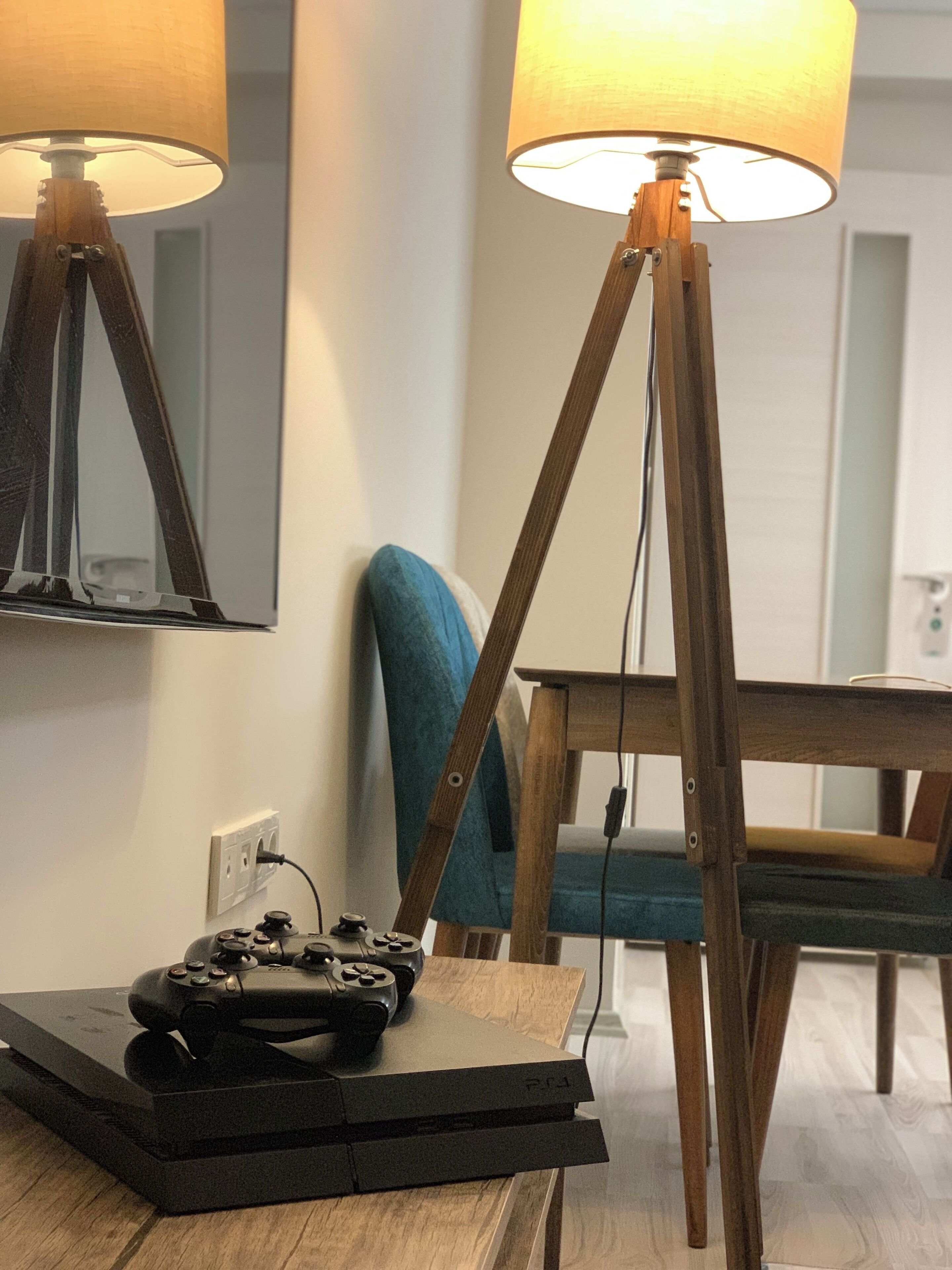 A room with a wooden table, a lamp, a chair, and a gaming console.