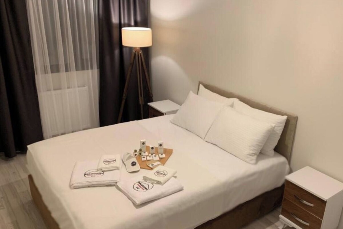 A neatly made bed with a white duvet, a bedside table with a lamp, and a small wooden nightstand.