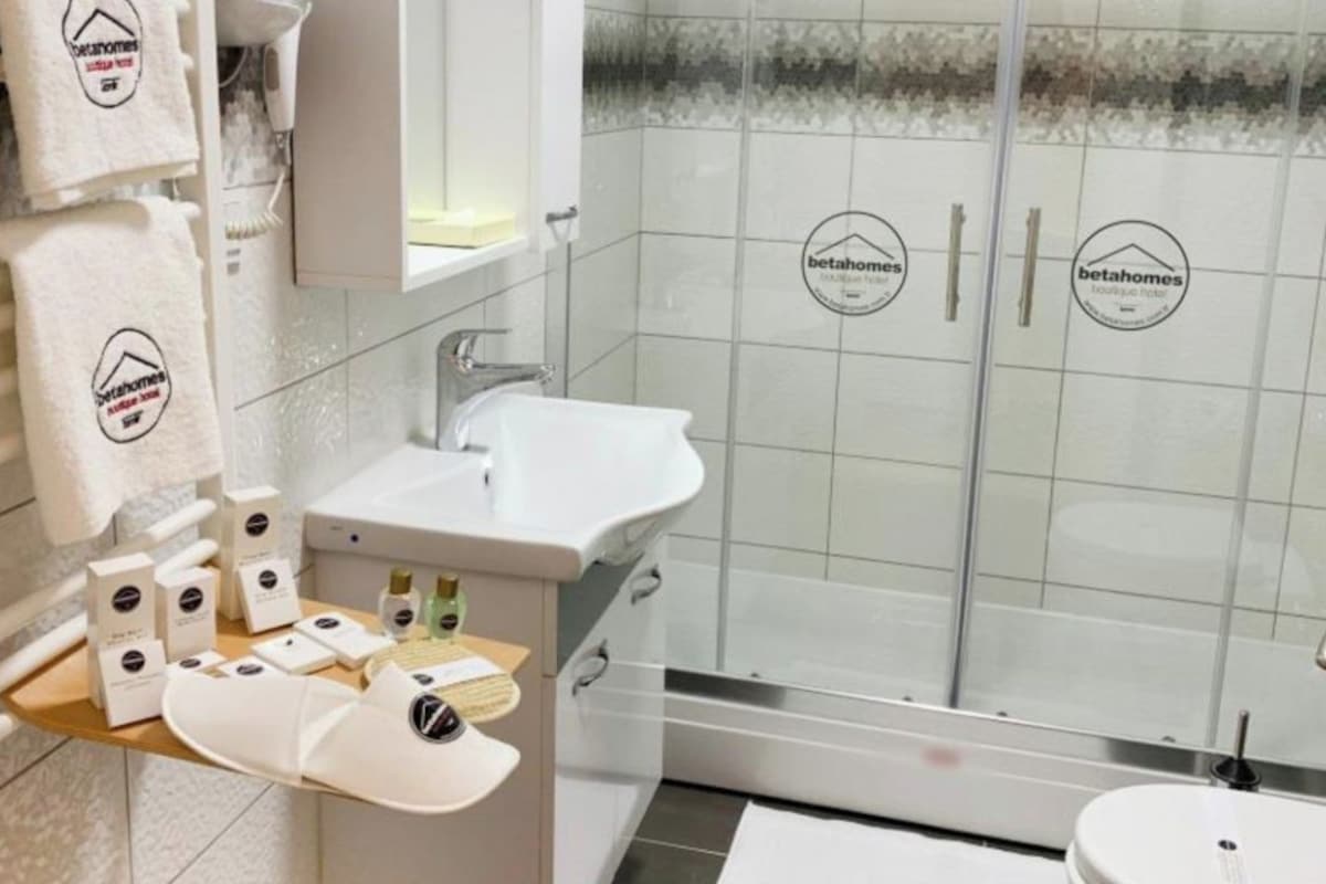 A modern bathroom with a glass shower, a sink, and a toilet. There are towels hanging on the wall and a small shelf with toiletries.