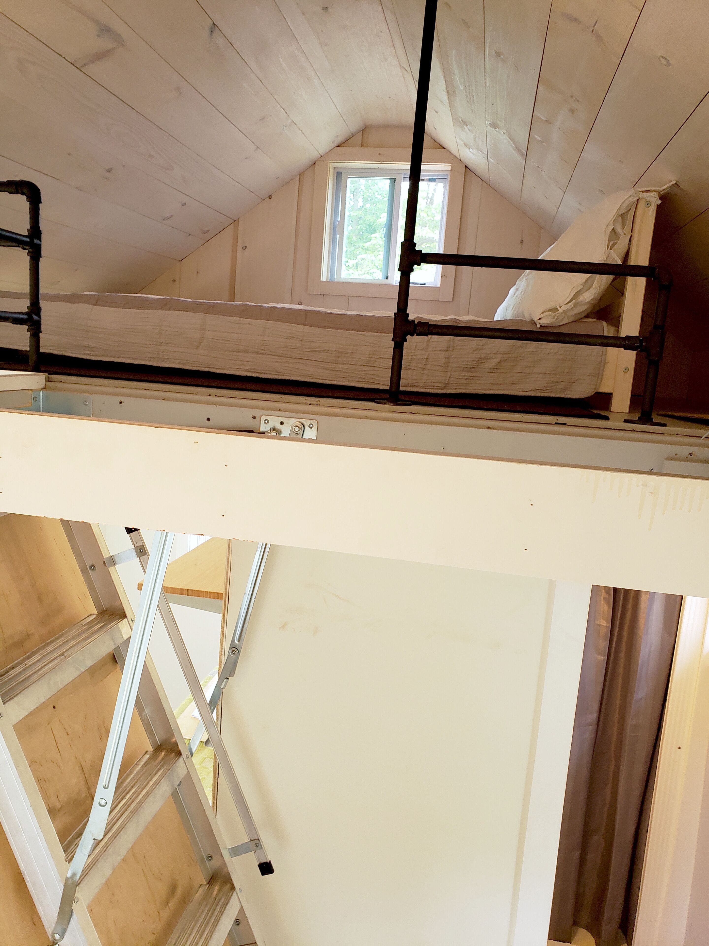 Une chambre à coucher aménagée dans un grenier, avec un lit superposé, des poutres en bois et une fenêtre.