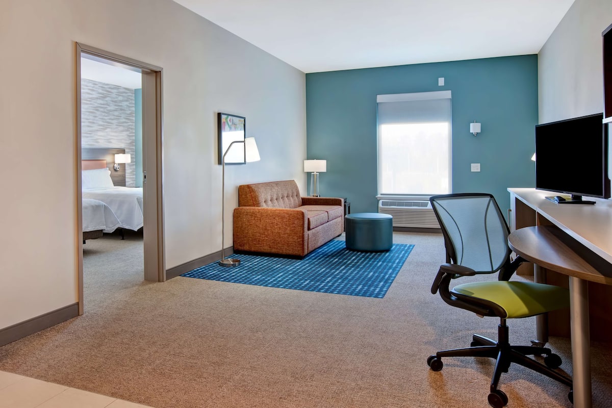 Ein Hotelzimmer mit Bett, braunem Sofa, Schreibtisch, Stuhl und Fernseher.