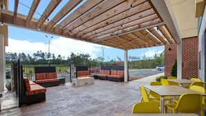 An outdoor patio with wooden flooring, yellow chairs, and a fire pit. - Home2 Suites by Hilton Charlotte Northlake (Charlotte)