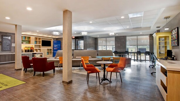 A modern hotel lobby with seating areas, a reception desk, and a bar. - Home2 Suites by Hilton Charlotte Northlake (Charlotte)