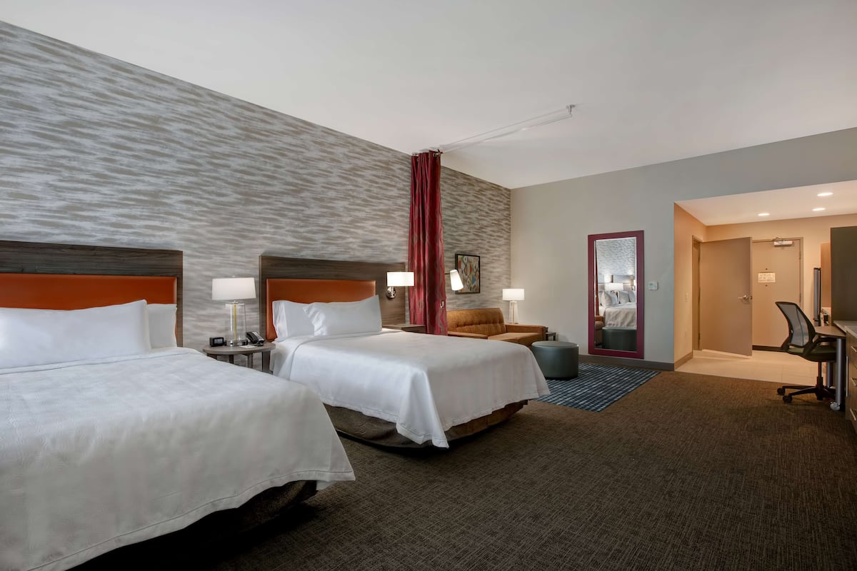 Ein Hotelzimmer mit zwei Betten, einem Schreibtisch, einem Stuhl, einer Lampe und einer Badezimmertür.