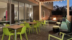 An outdoor patio area with tables and chairs, a fire feature, and a seating area with a patterned cushion. - Home2 Suites by Hilton Harrisburg North (Harrisburg)