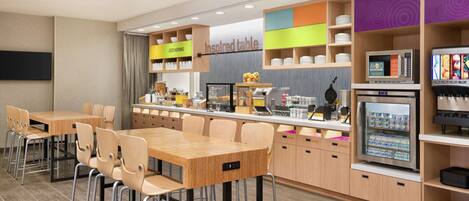 A modern kitchen area with a dining table and chairs, a coffee station, and a refrigerator.