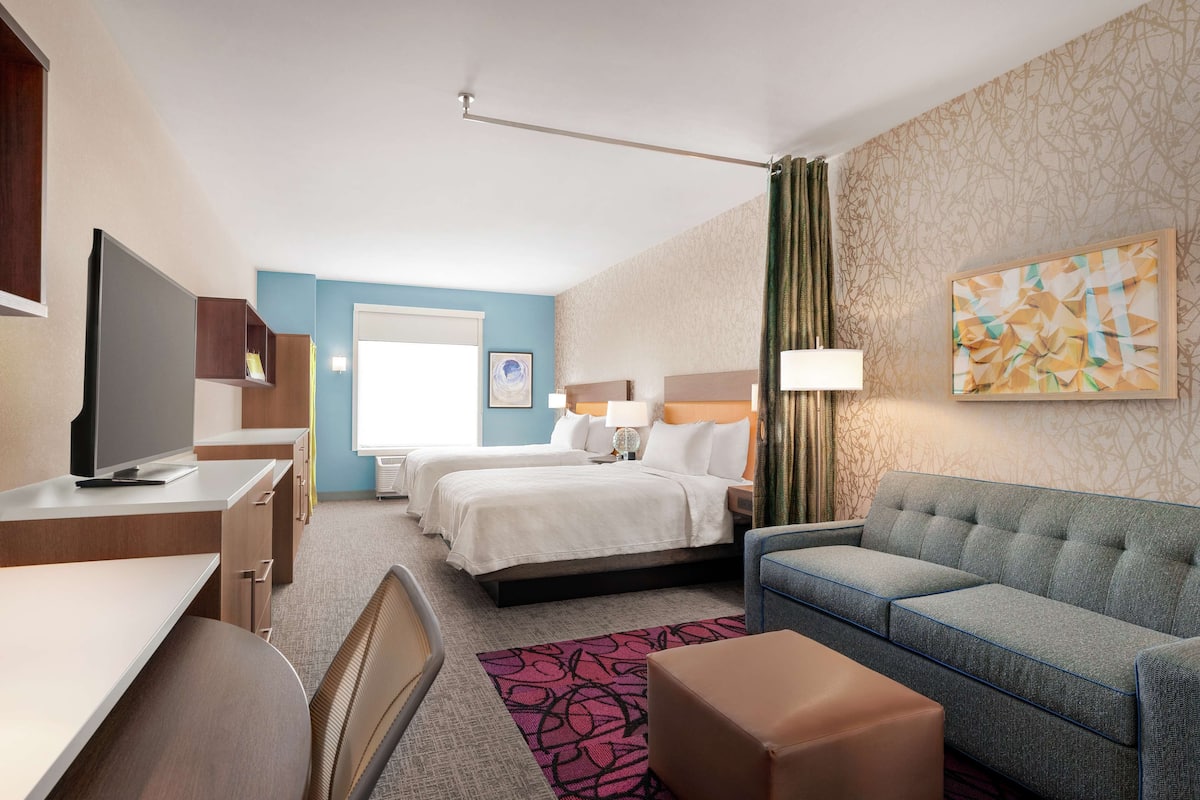 Une chambre d’hôtel équipée d’un bureau, de deux lits, d’un canapé et d’une télévision.