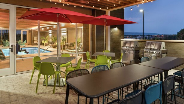 An outdoor patio with tables and chairs, a barbecue grill, and a pool. - Home2 Suites by Hilton Harrisburg North (Harrisburg)