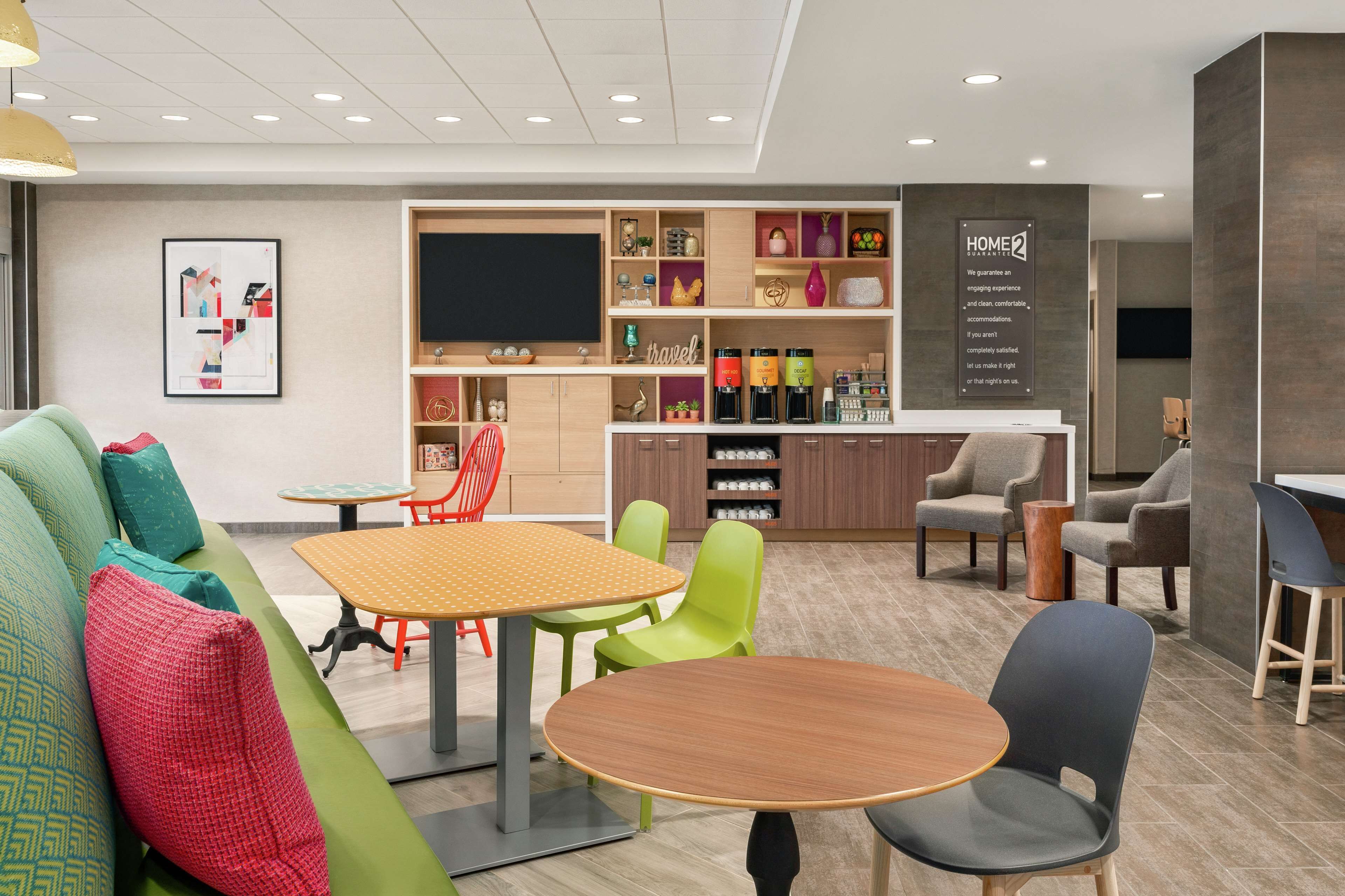A modern hotel lobby with a seating area, a coffee bar, and a television screen.