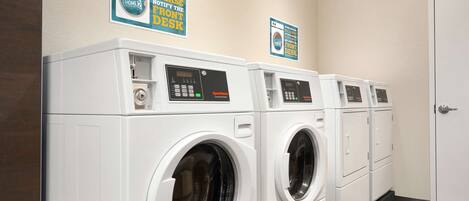 A laundry room with four front-loading washing machines, a door, and two signs on the wall.