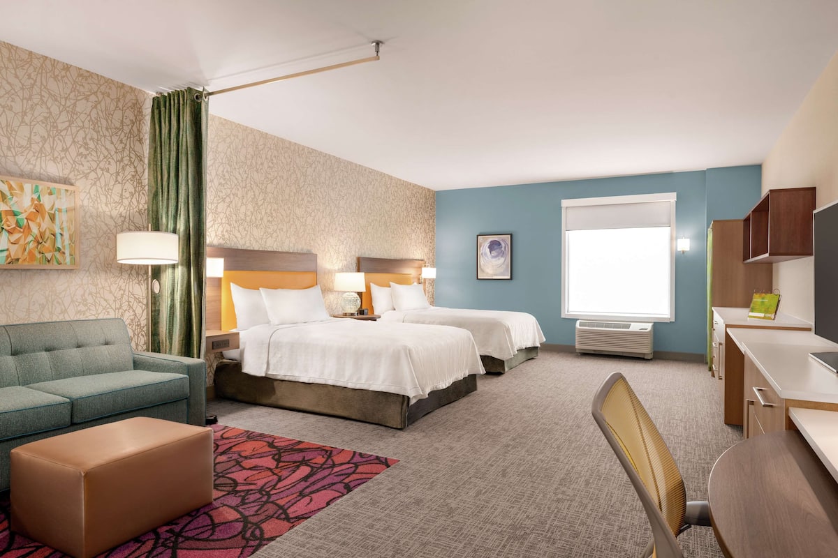 Une chambre d’hôtel avec deux lits, un bureau, une chaise, un canapé et une grande fenêtre.