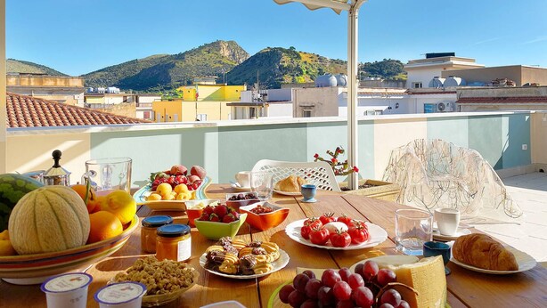 A table set for breakfast on a balcony with a view of buildings and hills. - Solemar Sicilia - Casa Enza (Santa Flavia)