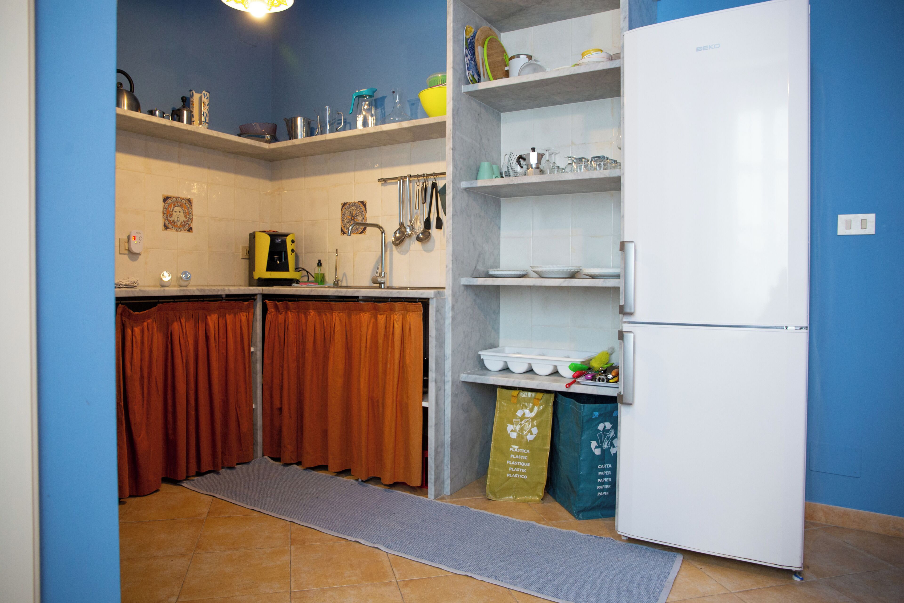 A kitchen with a white refrigerator, shelves with dishes, and a tiled backsplash.