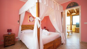 A bedroom with a four-poster bed, a wooden nightstand with a lamp, and a view of the outside through an open door. - Solemar Sicilia - Casa Enza (Santa Flavia)