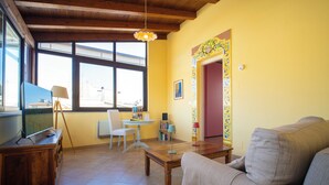 A living room with a wooden ceiling, a sofa, a coffee table, a TV, and a dining area with a table and chairs. - Solemar Sicilia - Casa Enza (Santa Flavia)