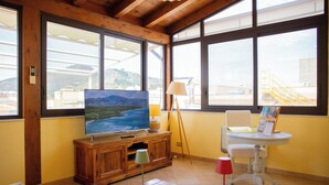 A living room with a TV, wooden cabinet, lamp, and a table with a chair. - Solemar Sicilia - Casa Enza (Santa Flavia)
