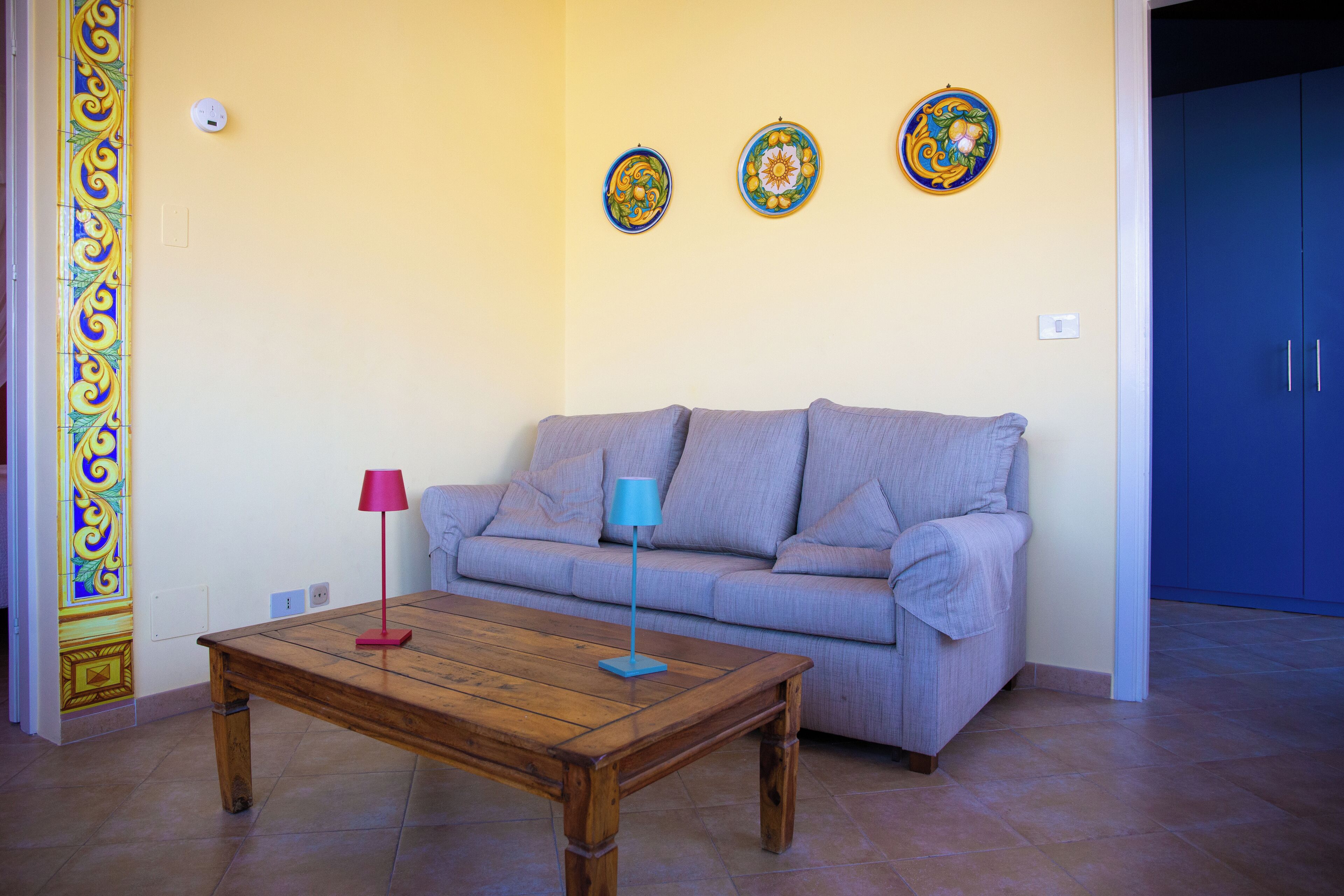 Ein Wohnzimmer mit Couchtisch aus Holz, einer grauen Couch und drei dekorativen Tellern an der Wand.