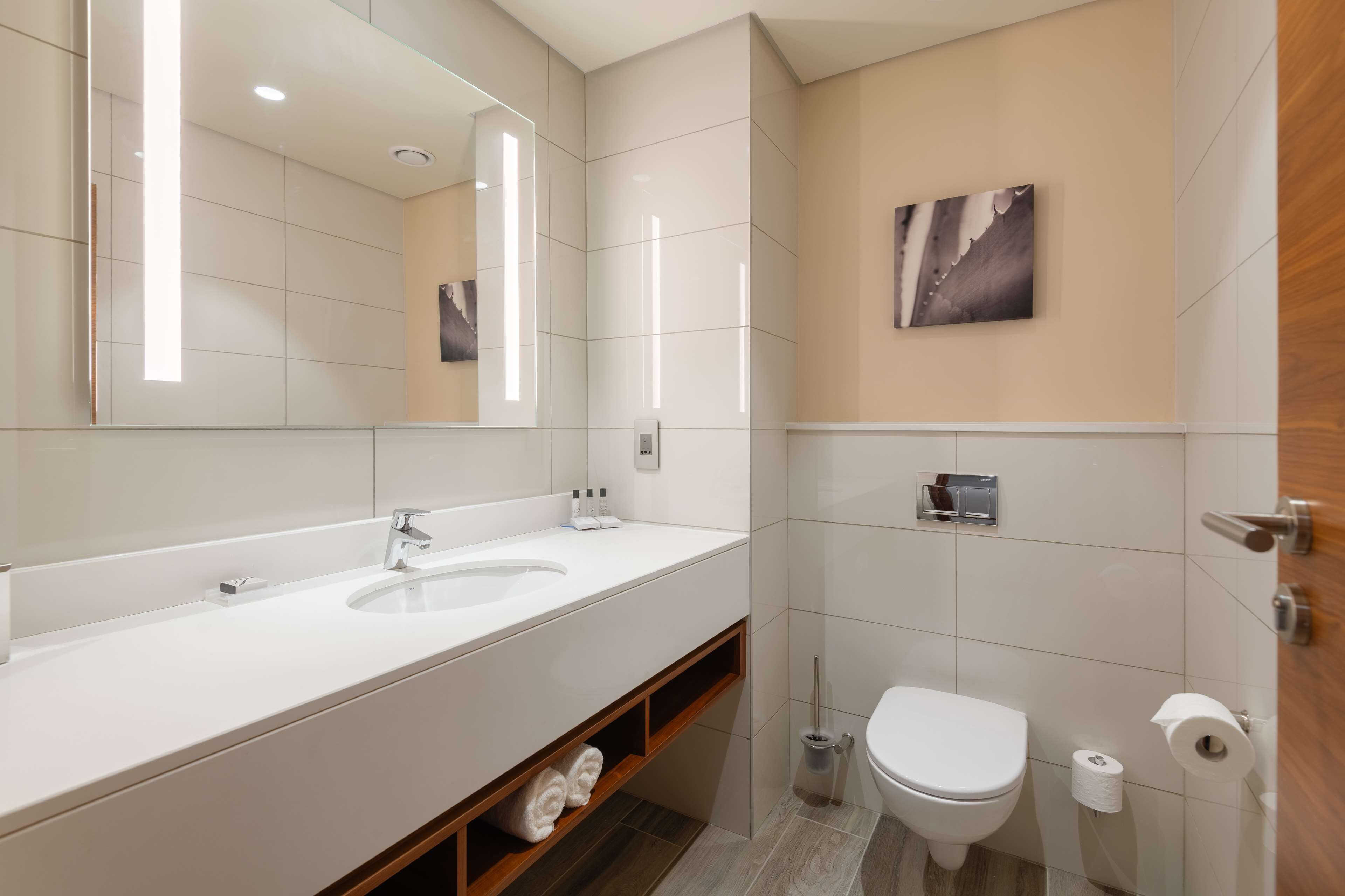 Un baño moderno con un espejo grande, dos lavamanos, un inodoro y una zona de ducha.