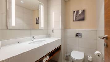 A modern bathroom with a large mirror, two sinks, a toilet, and a shower area.