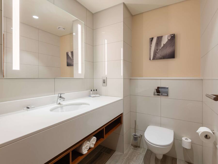 A modern bathroom with a large mirror, two sinks, a toilet, and a shower area.