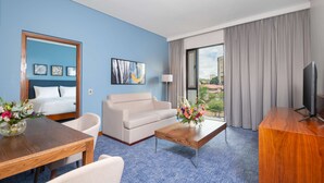 A hotel room with a bed, a sofa, a coffee table, a TV, and a view of the outside. - Hilton Garden Inn Windhoek (Windhoek)