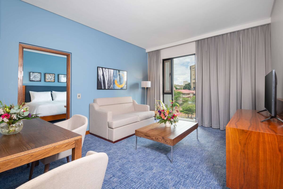 A hotel room with a bed, a sofa, a coffee table, a TV, and a view of the outside.