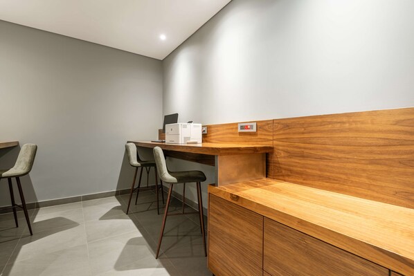 Un área de recepción con un mostrador de madera, dos taburetes de bar y un escritorio pequeño con una impresora.