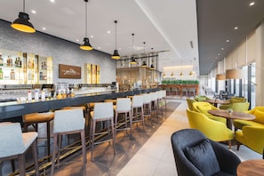 Zona de bar moderna con una barra larga, varios taburetes y una gran variedad de botellas.