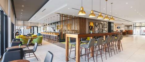 Un restaurante moderno con barra, mesas y sillas, y una pared decorativa.