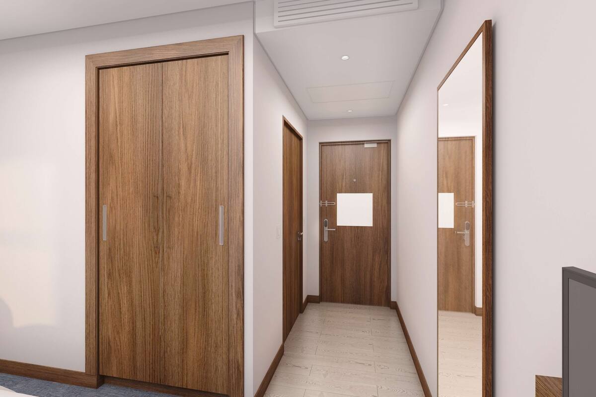 A hotel corridor with wooden doors, a tiled floor, and a flat ceiling with recessed lighting.